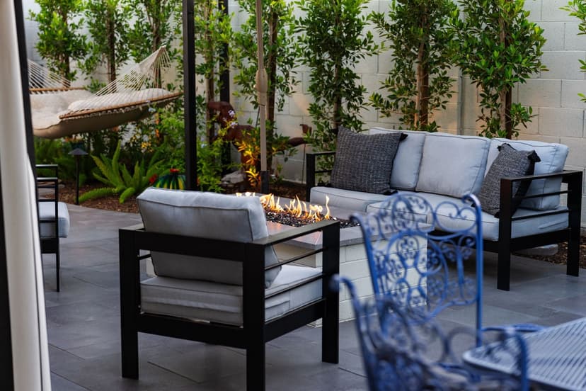 Elegant outdoor seating area with fire pit, lush greenery, and a hammock for relaxation.