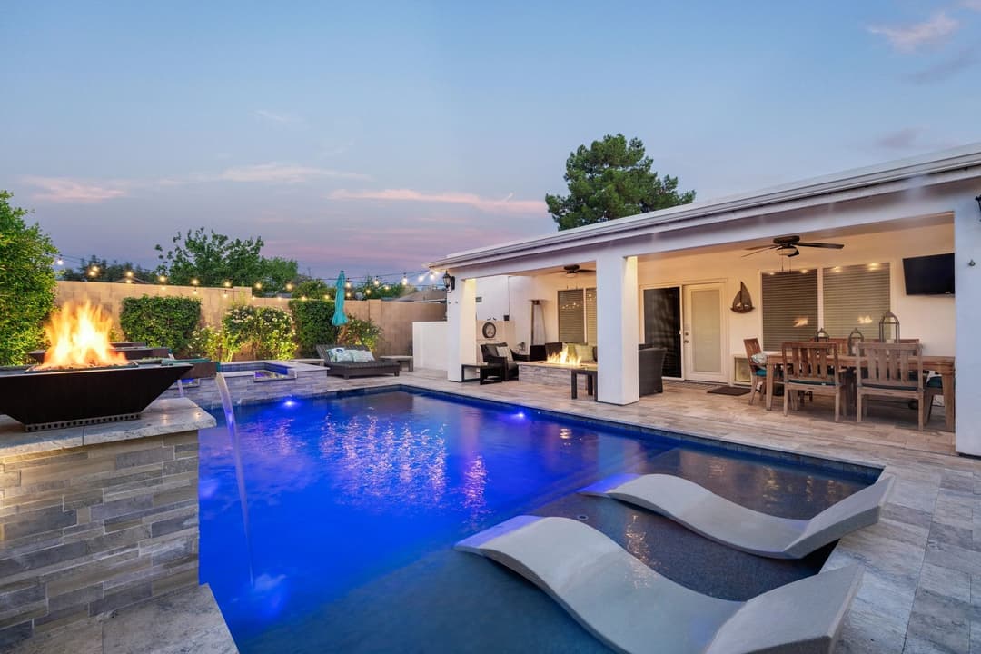Modern backyard oasis with pool, lounge chairs, fire pit, and outdoor dining area at dusk.
