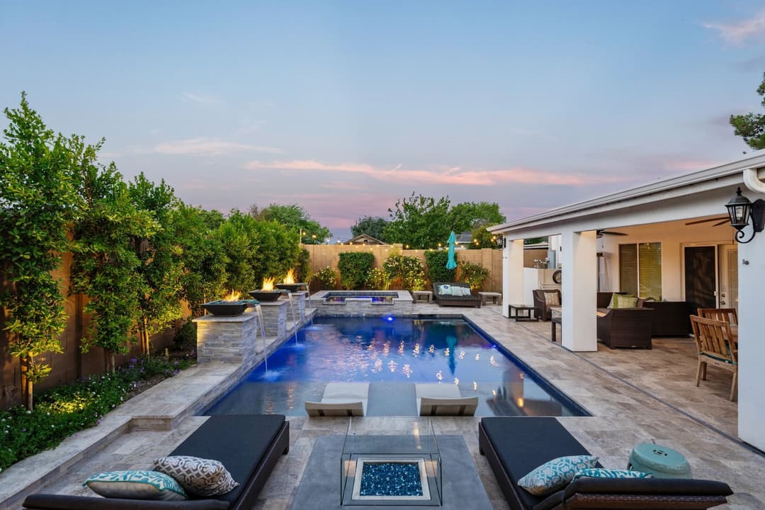 Modern backyard with swimming pool, lounge chairs, and landscaped greenery at sunset.