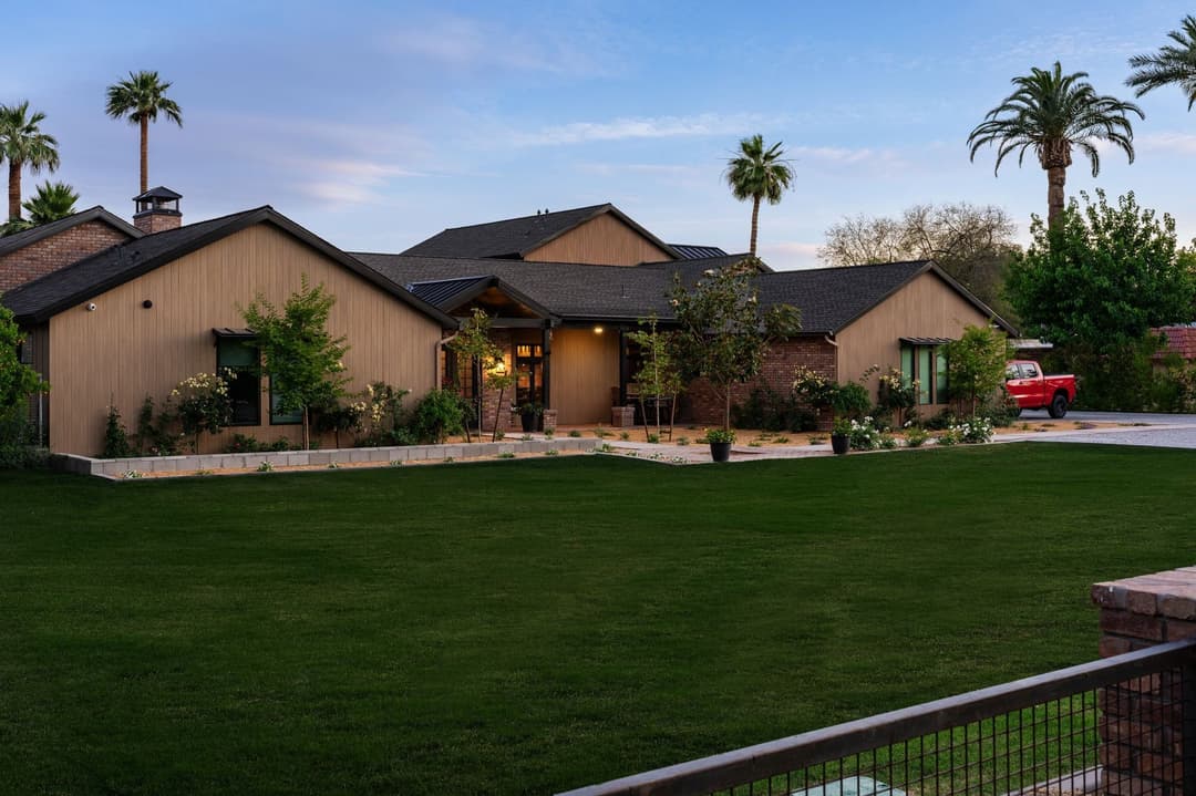 Modern ranch-style home with a lush green lawn and palm trees under a clear sky.
