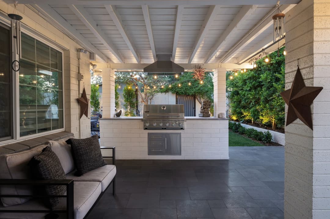 Modern outdoor kitchen with grill, seating area, and garden in a stylish patio setting.