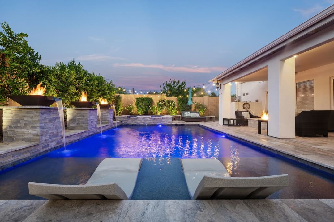 Luxury backyard pool with modern design, fire features, and relaxing seating area at dusk.