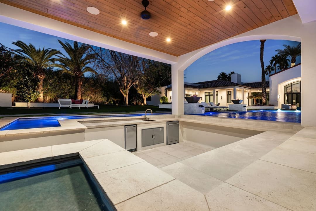 Modern outdoor living space with a luxurious pool, palm trees, and elegant patio lighting.