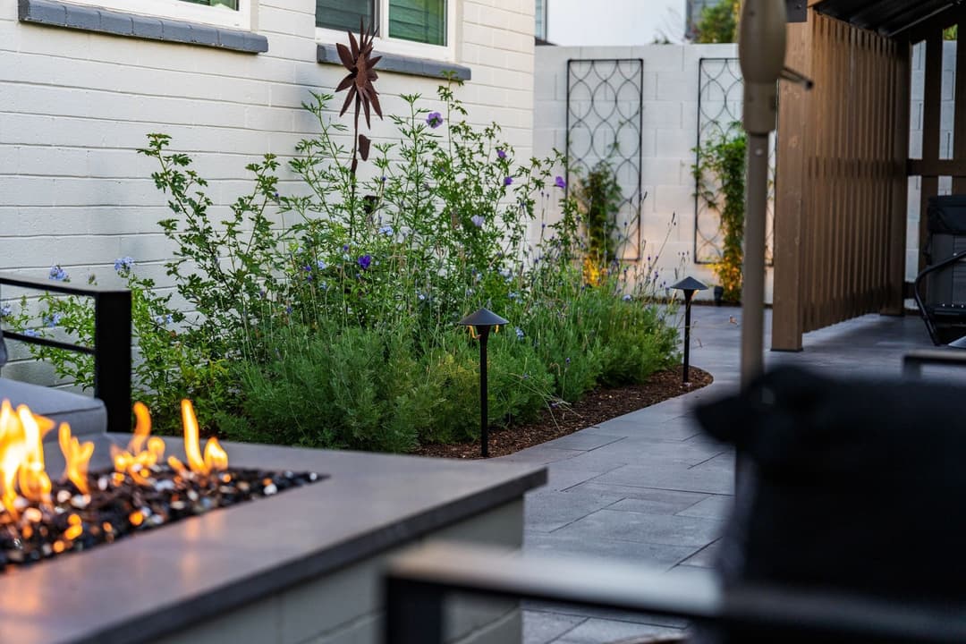 Modern outdoor space with a fire pit and lush garden, featuring elegant lighting at dusk.