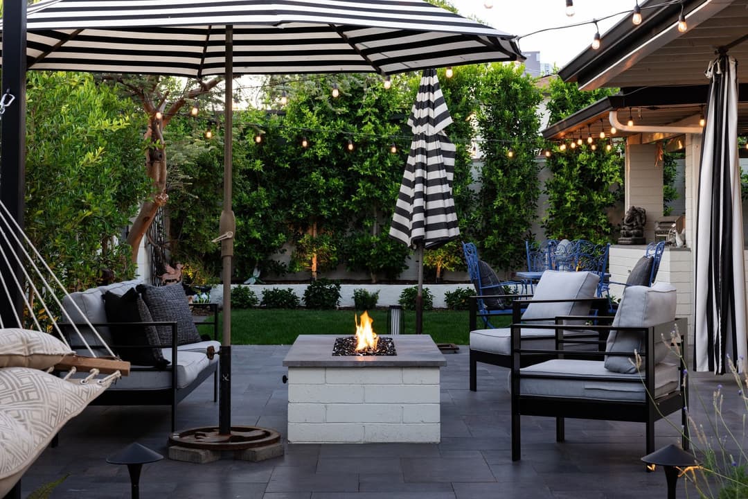 Stylish outdoor patio with black and white decor, fire pit, and lush green landscaping.