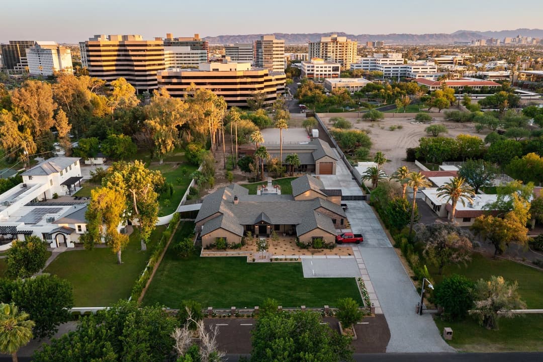 Aerial view of a luxury home surrounded by greenery and urban skyline in the background.