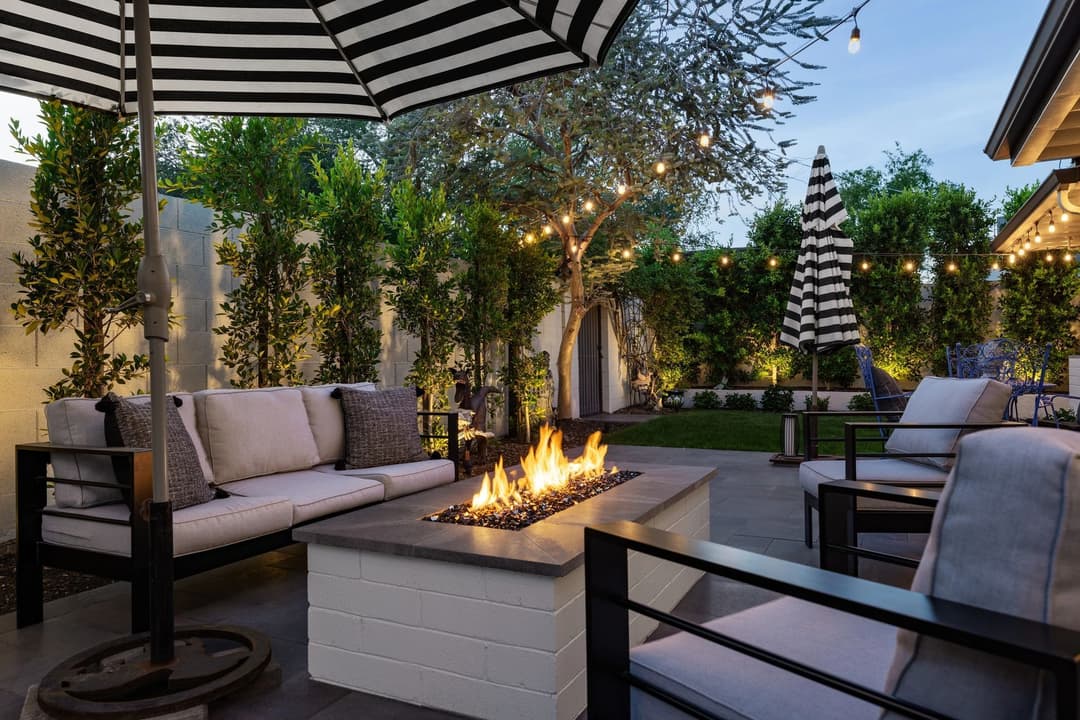 Cozy outdoor living space with fire pit, modern seating, and striped umbrellas at dusk.
