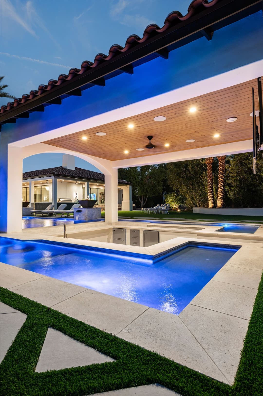 Modern outdoor pool area featuring a sleek design, spa, and lush landscaping at twilight.