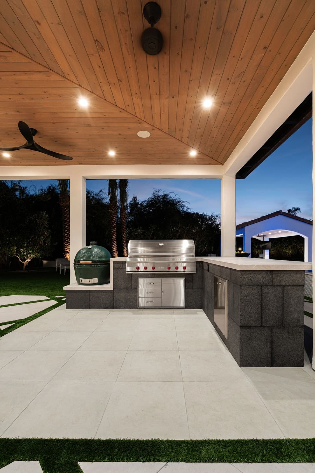 Modern outdoor kitchen featuring a stainless steel grill, green egg smoker, and sleek patio design.