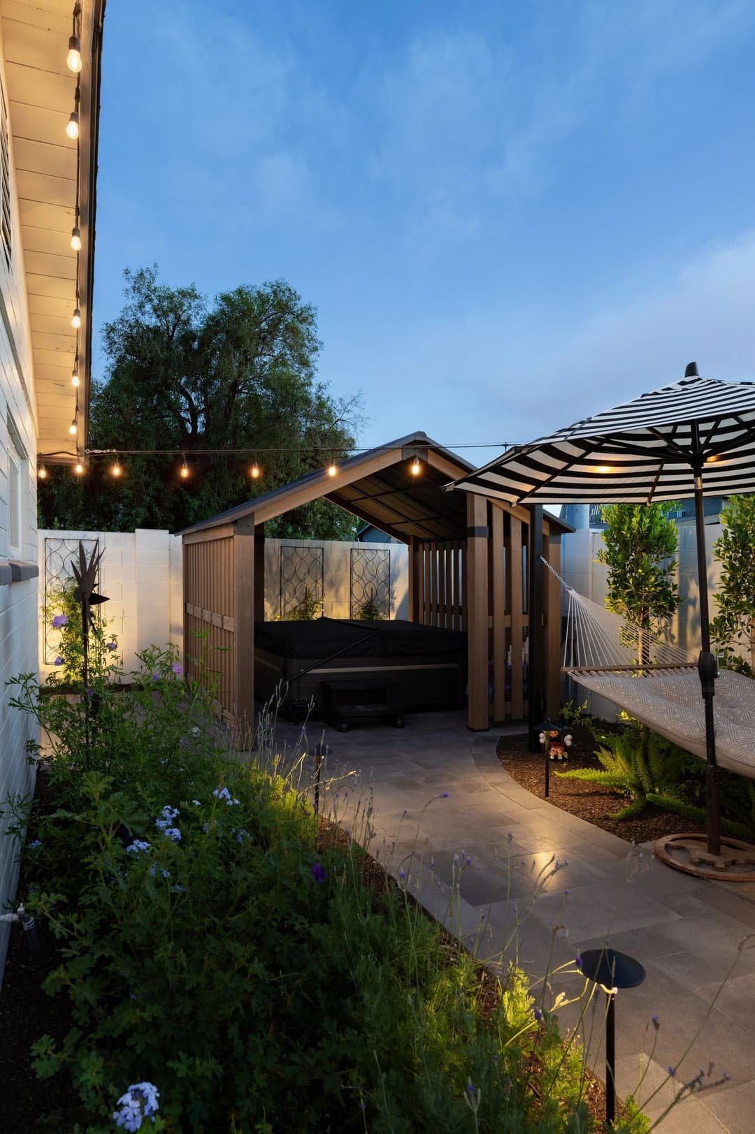 Cozy outdoor patio with warm lights, seating area, and lush greenery at dusk.
