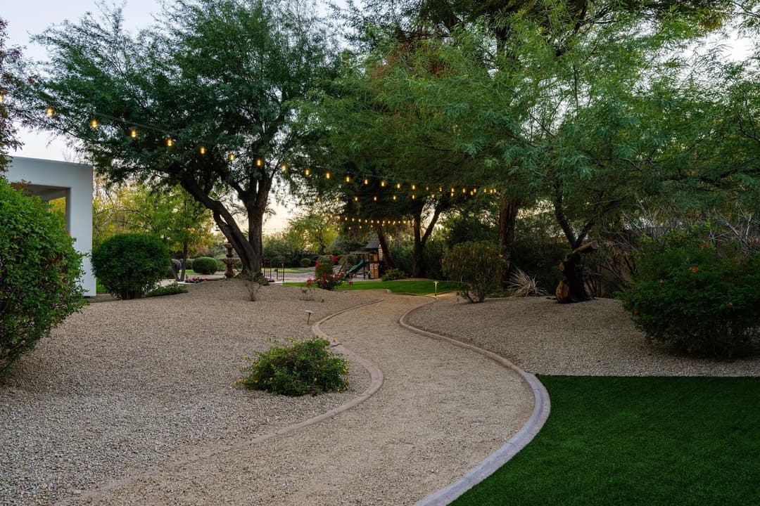 Scenic desert garden with a winding path, string lights, and lush greenery at sunset.