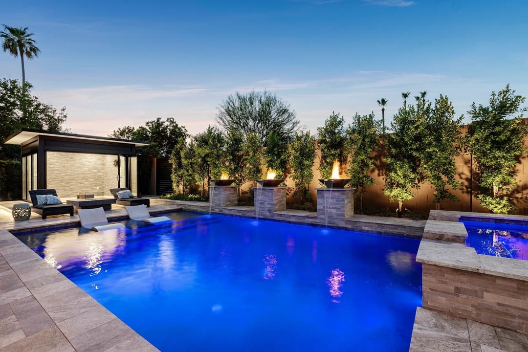 Luxury backyard pool with water features, lounge chairs, and modern landscaping at sunset.