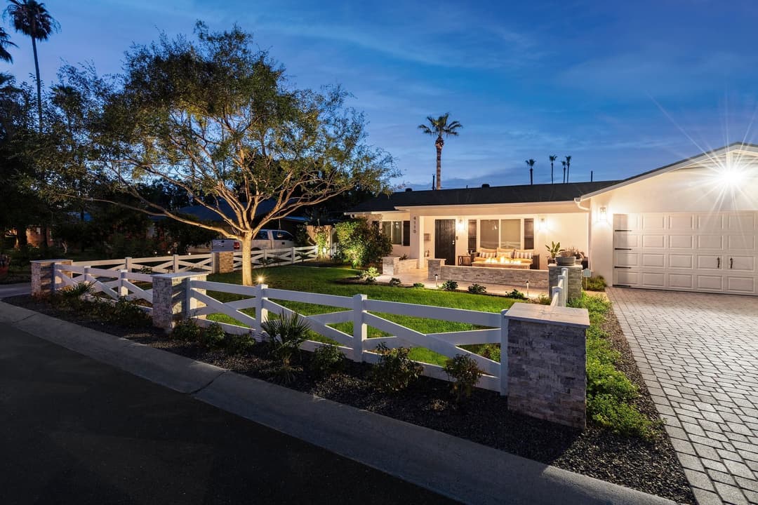 Charming home at dusk with white picket fence, lush lawn, and welcoming porch seating.