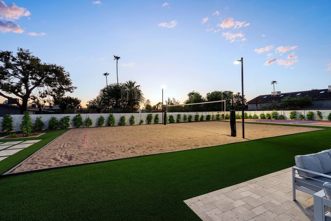 Beach volleyball court at sunset with lush greenery and modern landscaping elements.