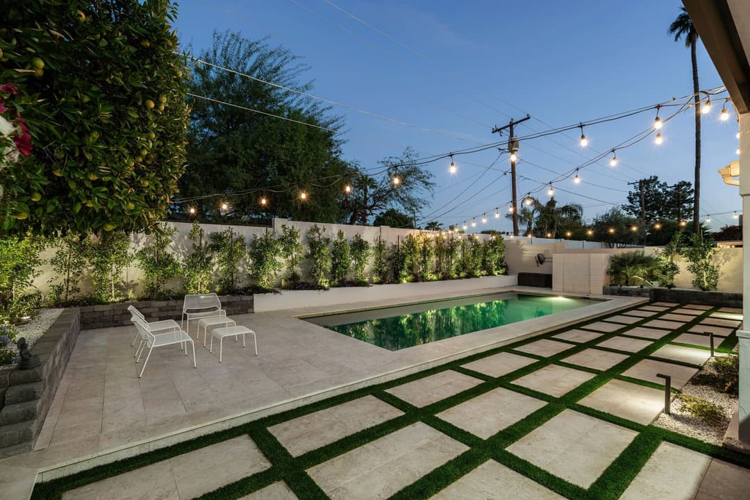 Modern backyard featuring a lit pool area, stylish seating, and landscaped greenery at dusk.