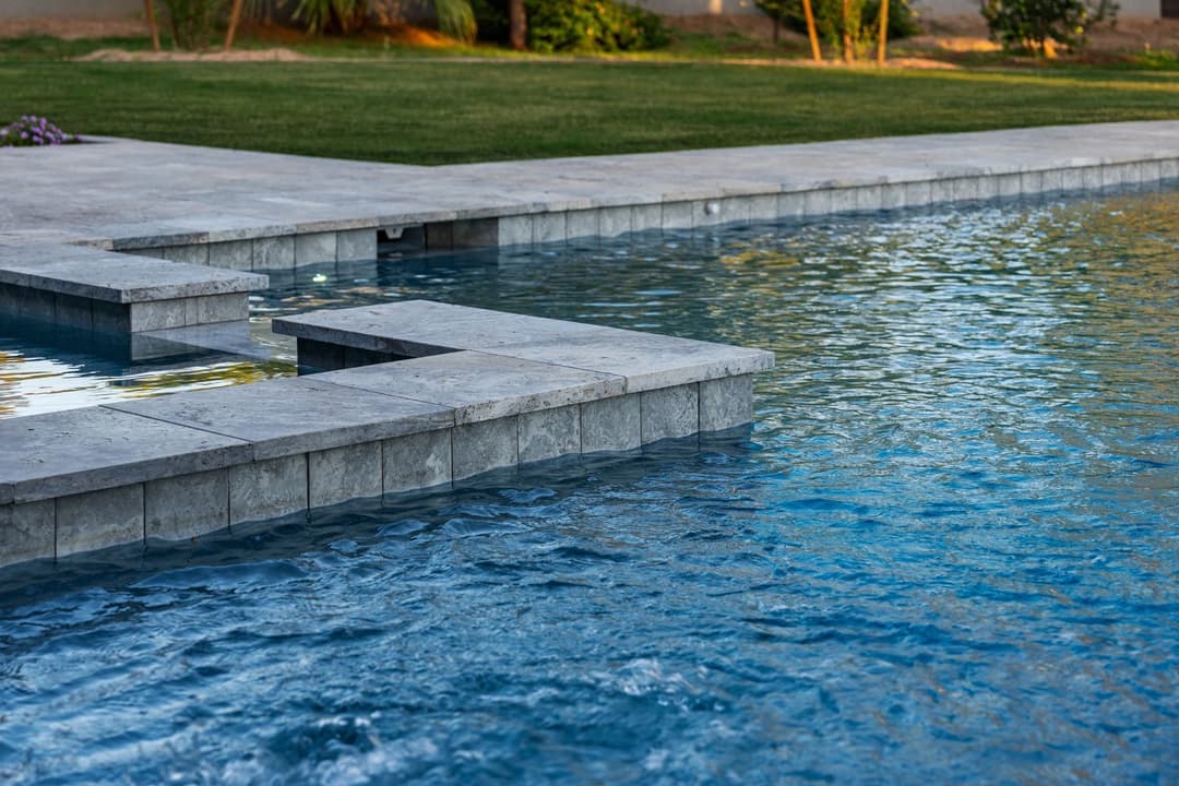 Modern backyard pool with stone edge reflecting sunlight on clear water surface.