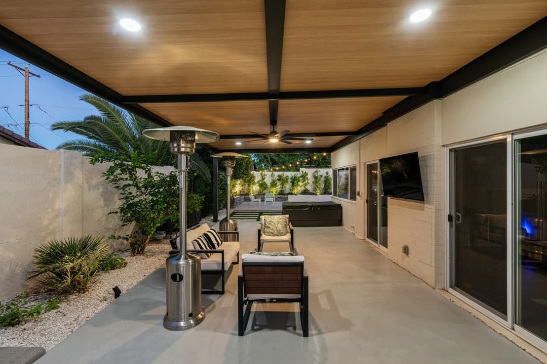 Modern outdoor patio with seating, heating lamps, and lush greenery at dusk.
