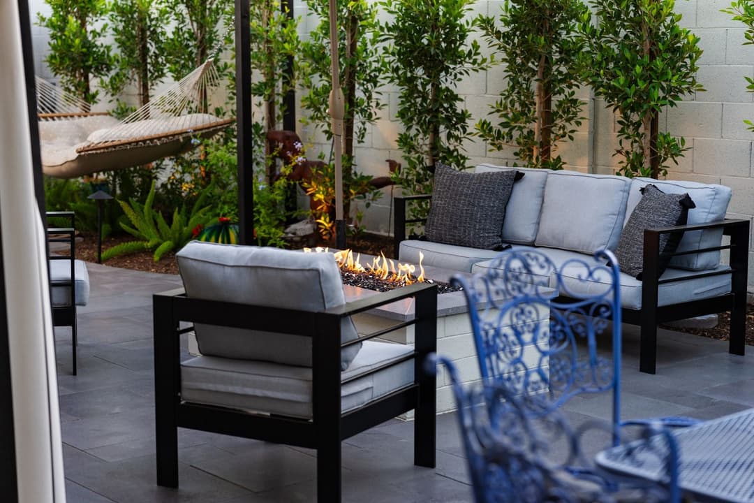 Modern outdoor patio with fire pit, cozy seating, and hammock surrounded by greenery.
