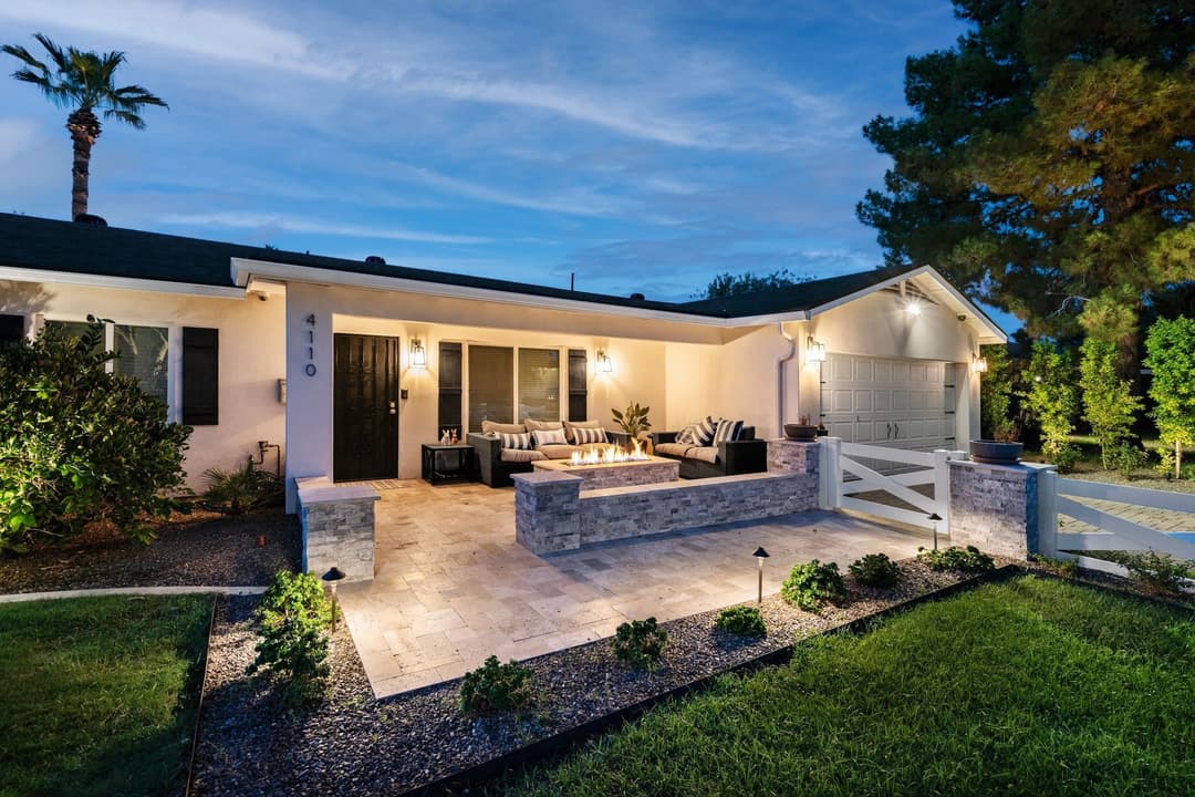 Modern home exterior with cozy patio, stone accents, and landscaped garden at dusk.