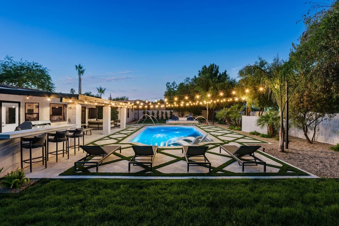 Modern backyard oasis with a sparkling pool, lounge chairs, and string lights at dusk.