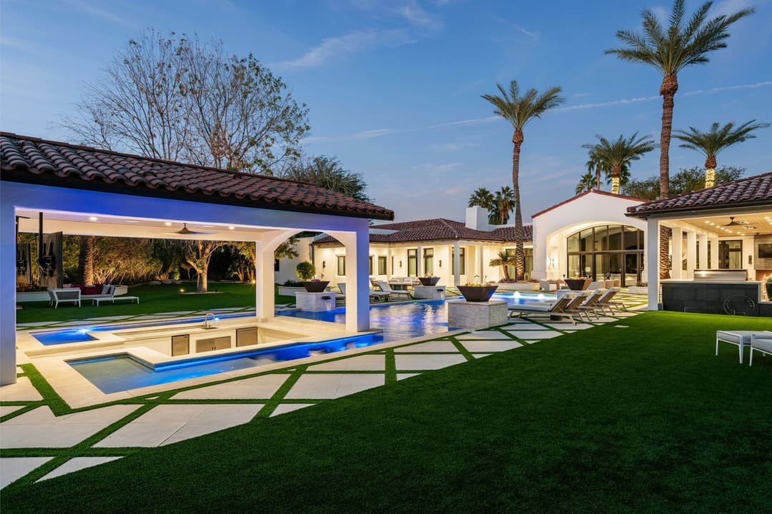 Luxury villa exterior with pool, spa, and palm trees at dusk, featuring modern landscaping.
