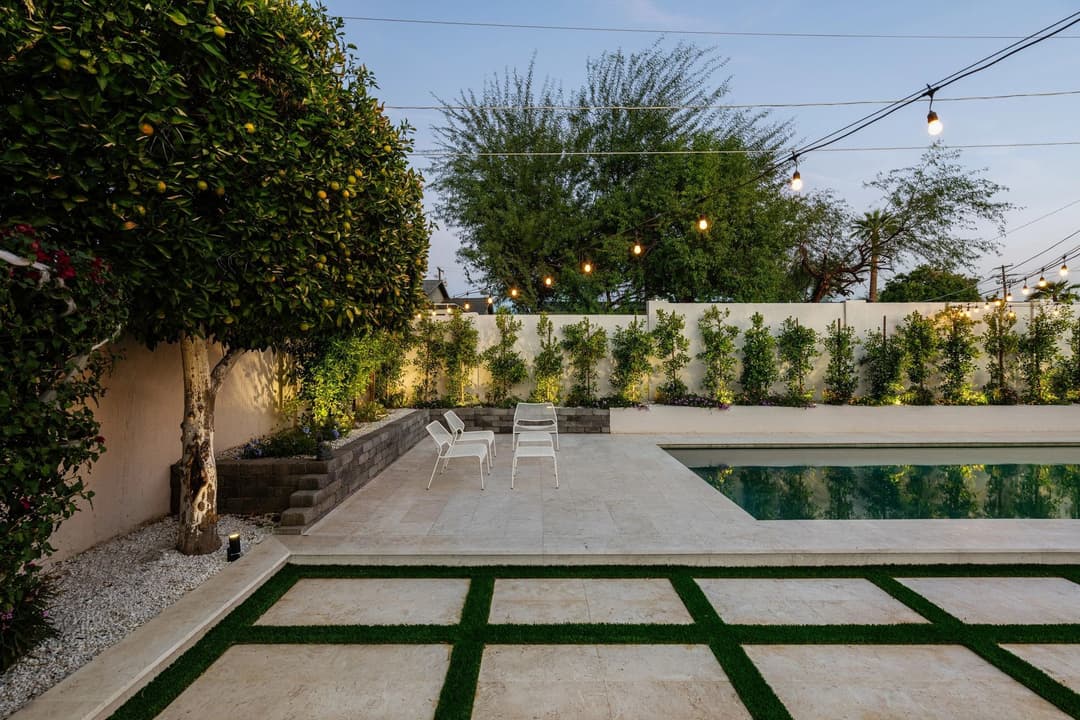 Modern backyard with pool, lush greenery, and string lights for ambiance.