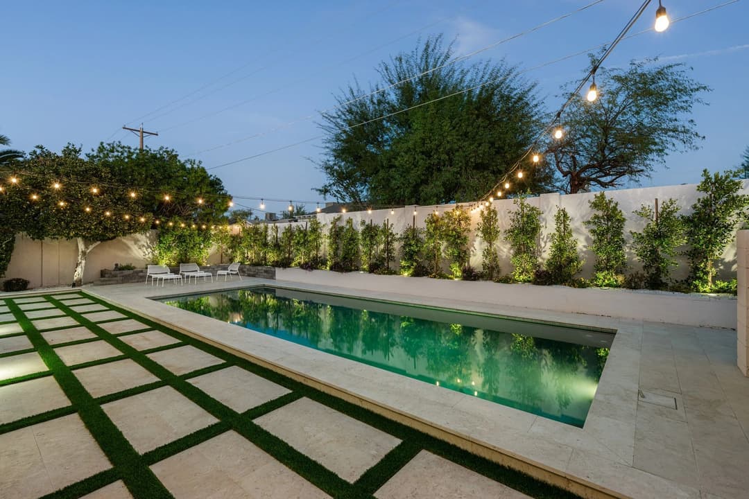 Modern backyard with a swimming pool, decorative lights, and landscaped greenery.